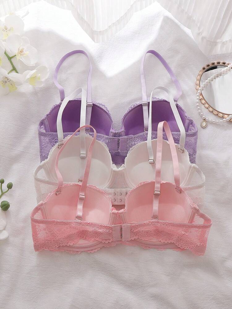 Set of three bras in purple, white, and pink on a white background with flowers and jewelry.