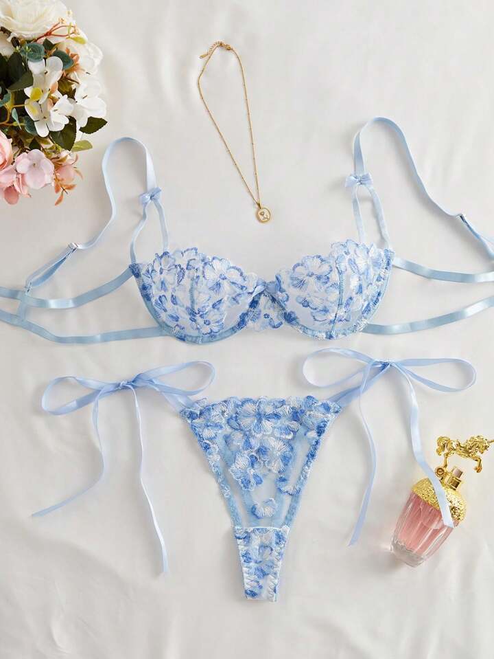 Blue floral lingerie set with a necklace and perfume bottle on a light background