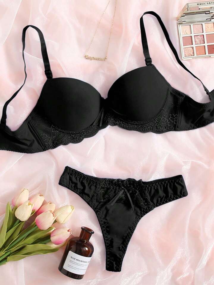 Black bra and panties set on a pink fabric background with a bottle and flowers.