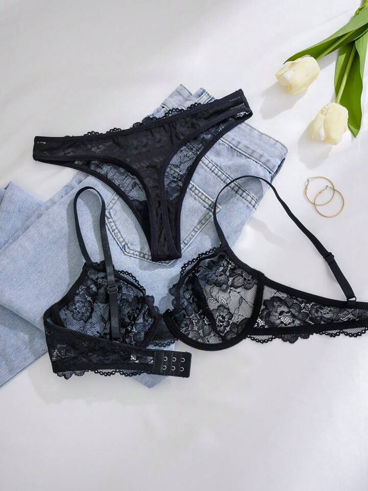 Black lace lingerie set on a light surface with flowers and denim jeans.