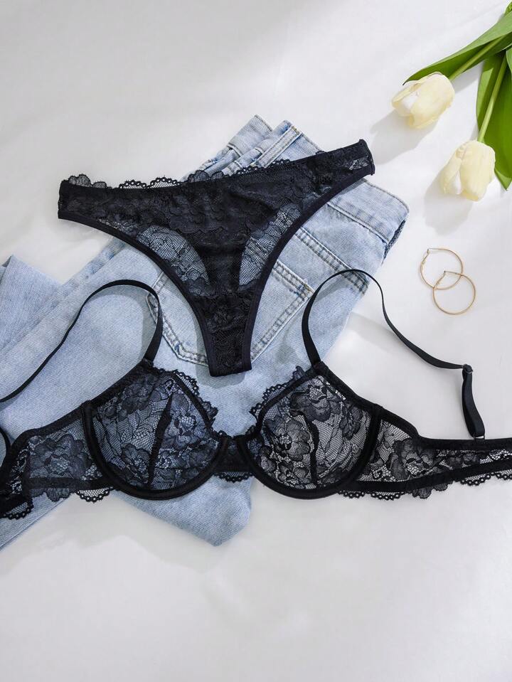 Black lace lingerie set on a white surface with tulips and jewelry.