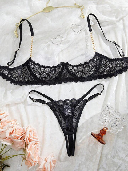 Black lace lingerie set on a textured white surface with flowers.