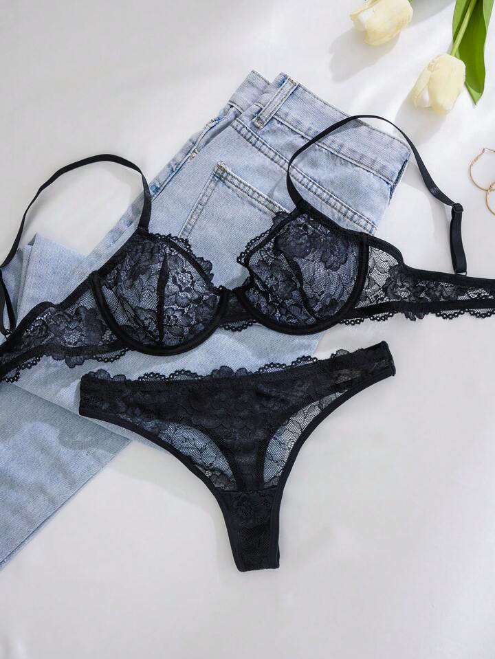 Black lace lingerie set with denim shorts on a white surface.