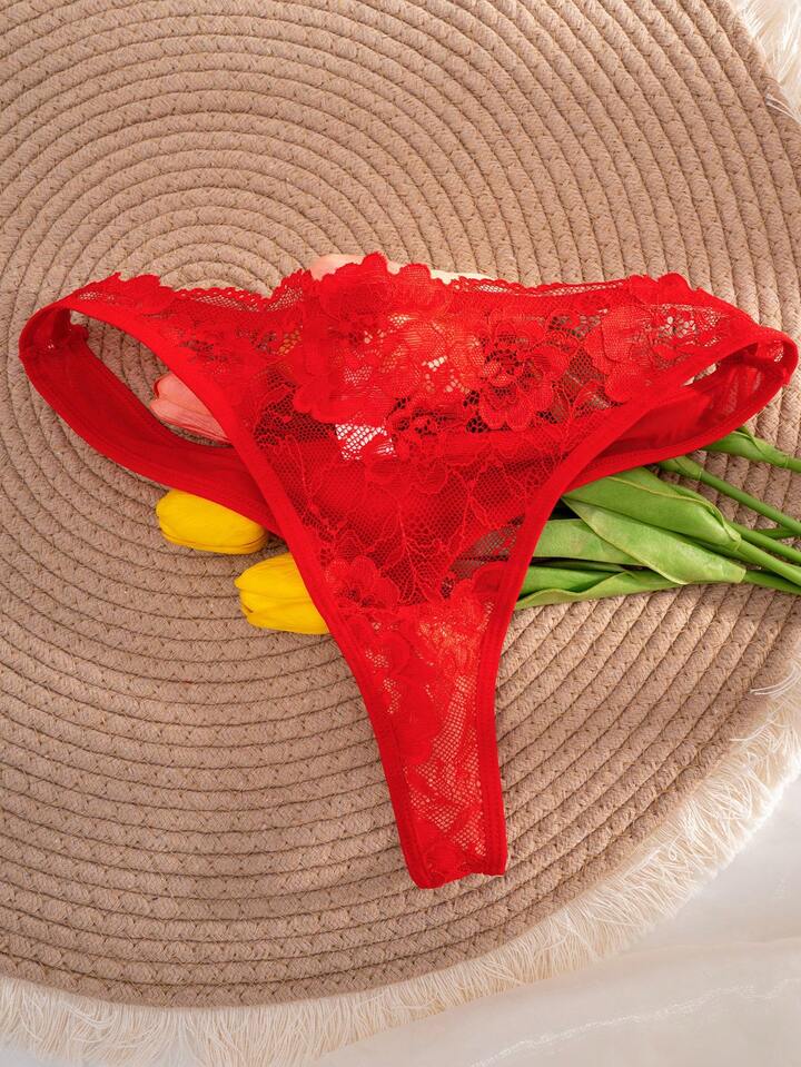 Red lace thong on a woven surface with flowers.