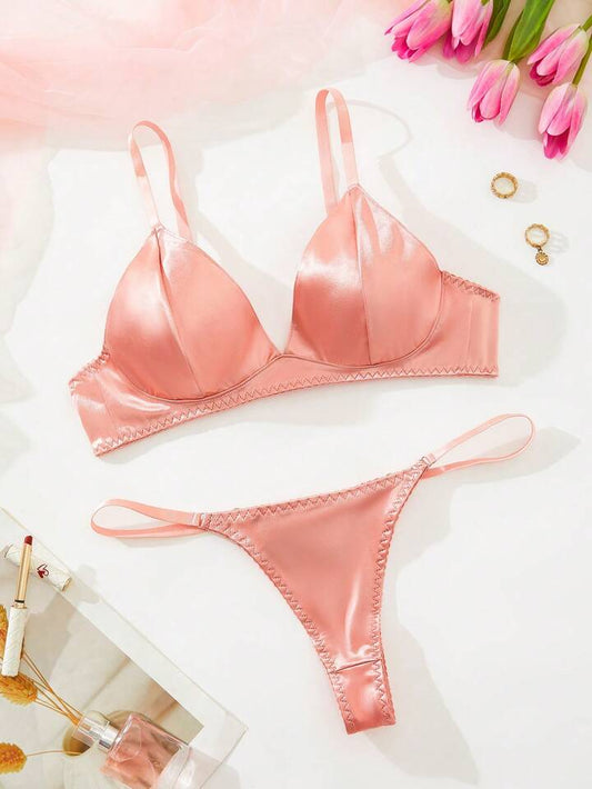 Pink satin bra and panties set on a white surface with pink tulips.