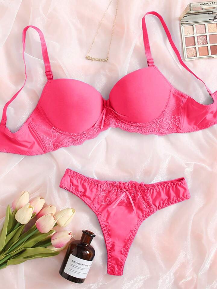 Pink bra and panties set on a soft pink background with flowers and a bottle.