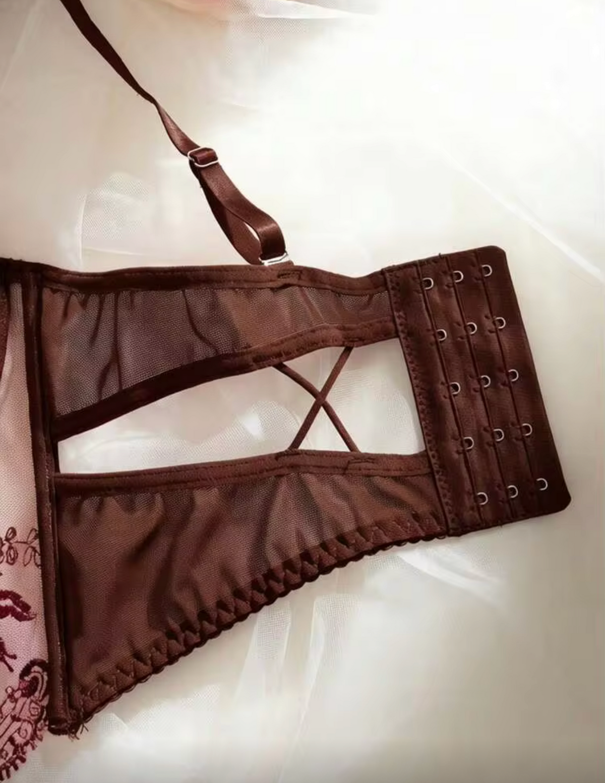 A brown lace-up lingerie bustier or corset-style undergarment laid flat on a white fabric surface, with side grommets and crisscross front straps visible.