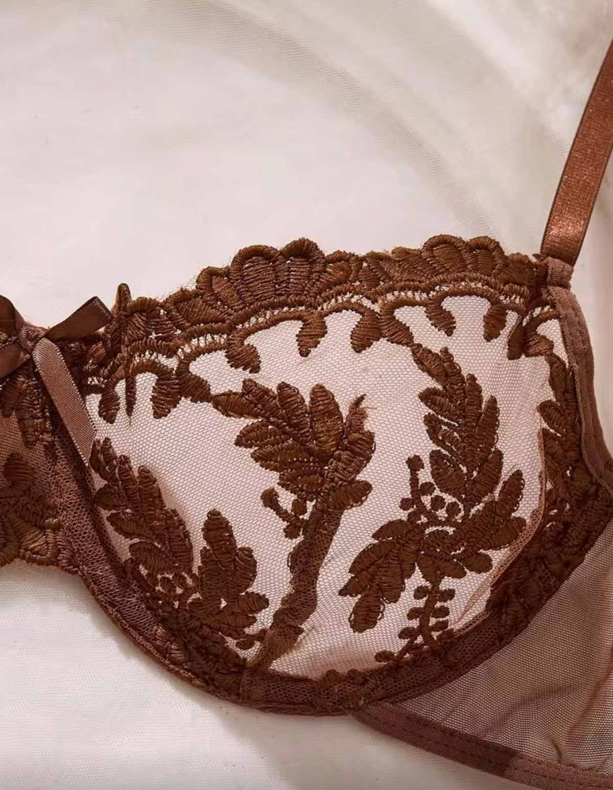 A close-up of a brown lace bra cup with floral embroidery on a light fabric background